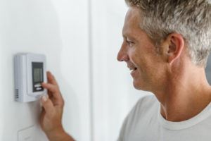 Middle-aged white man in white T-shirt adjusting thermostat.