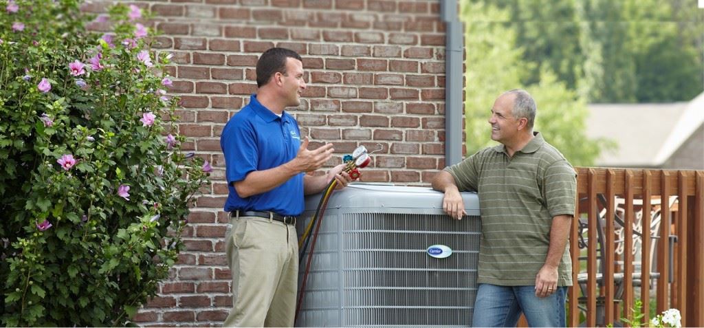 HVAC technician discussing SEER regulations outside next to AC unit with homeowner