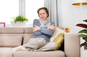 Woman sitting on couch, hugging her arms like she's cold.